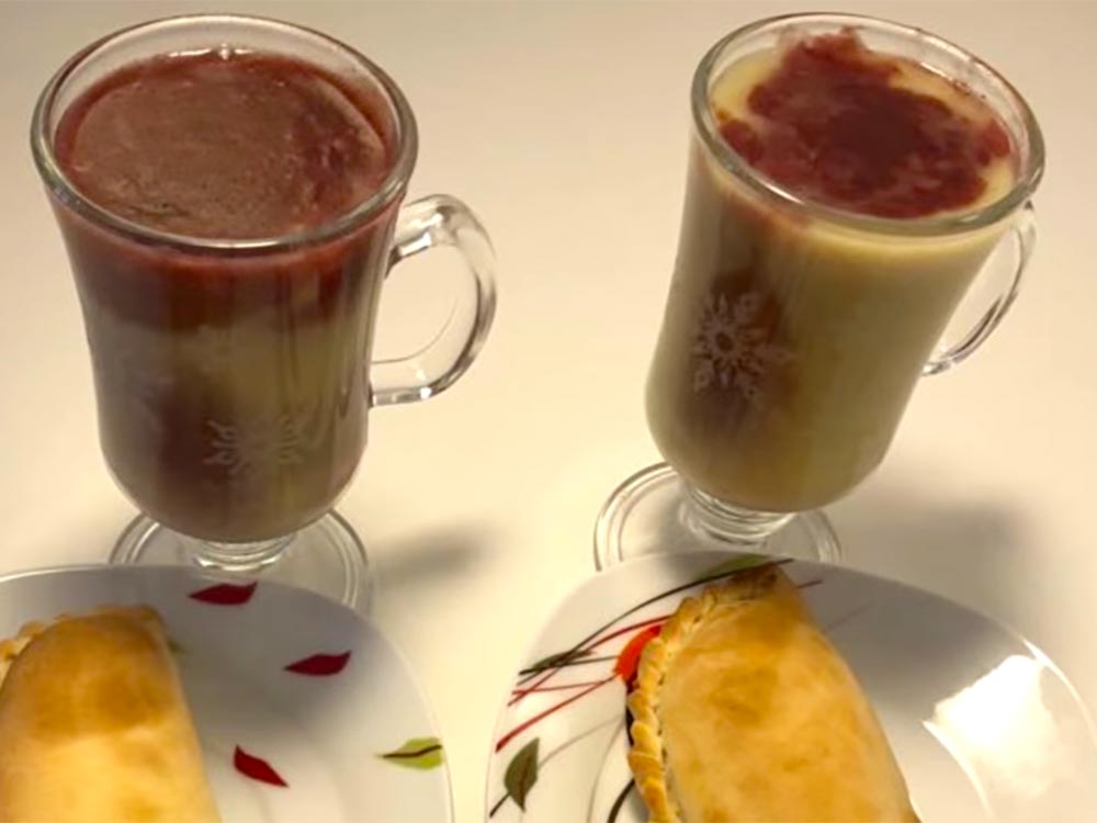Zwei Gläser mit dem bolivianischen Maisgetränk Api. Man sieht zwei Empanadas angeschnitten.
